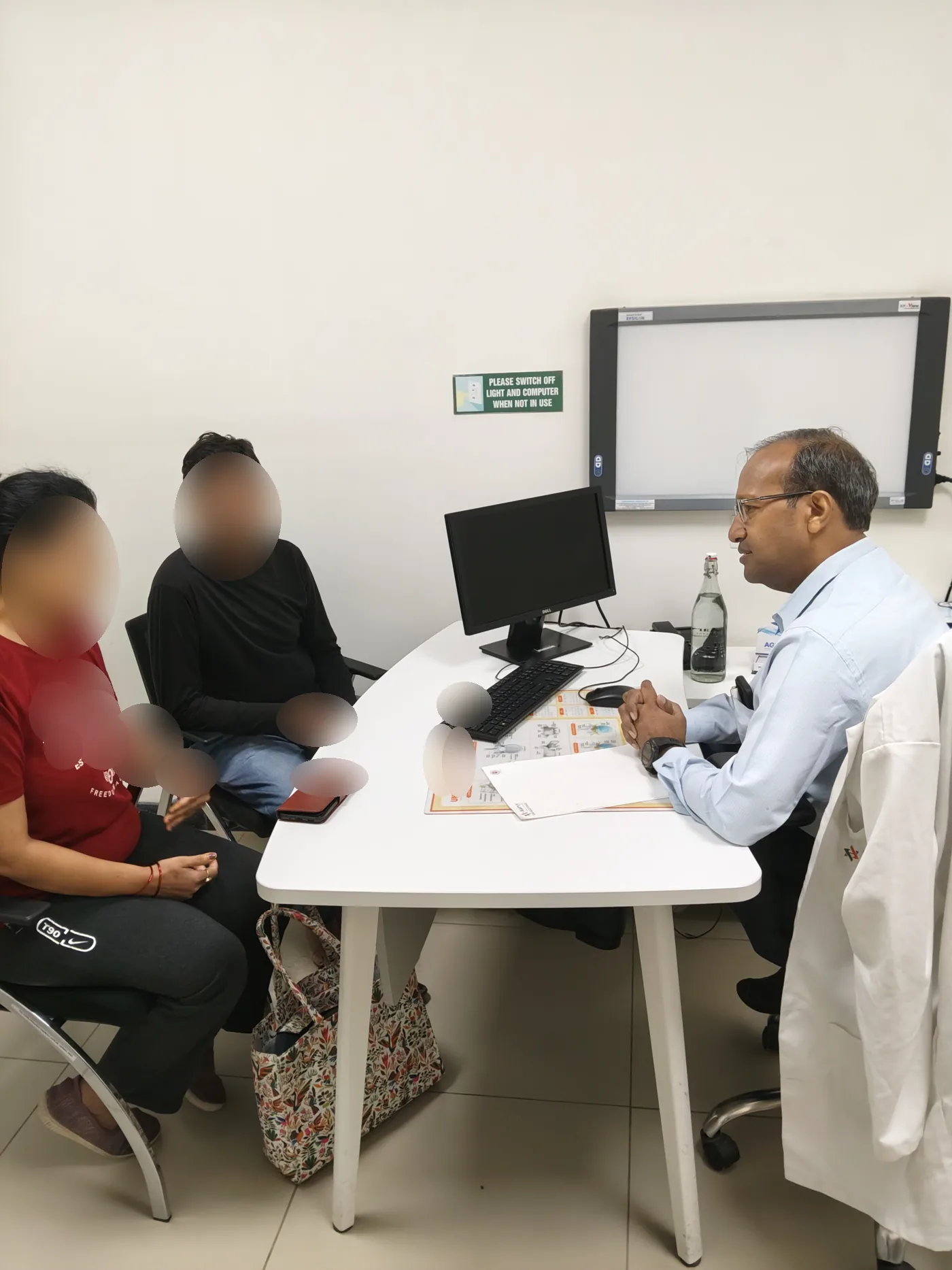Dr. Deepak Kumar speaking with a family in clinic. Patient faces are blurred.